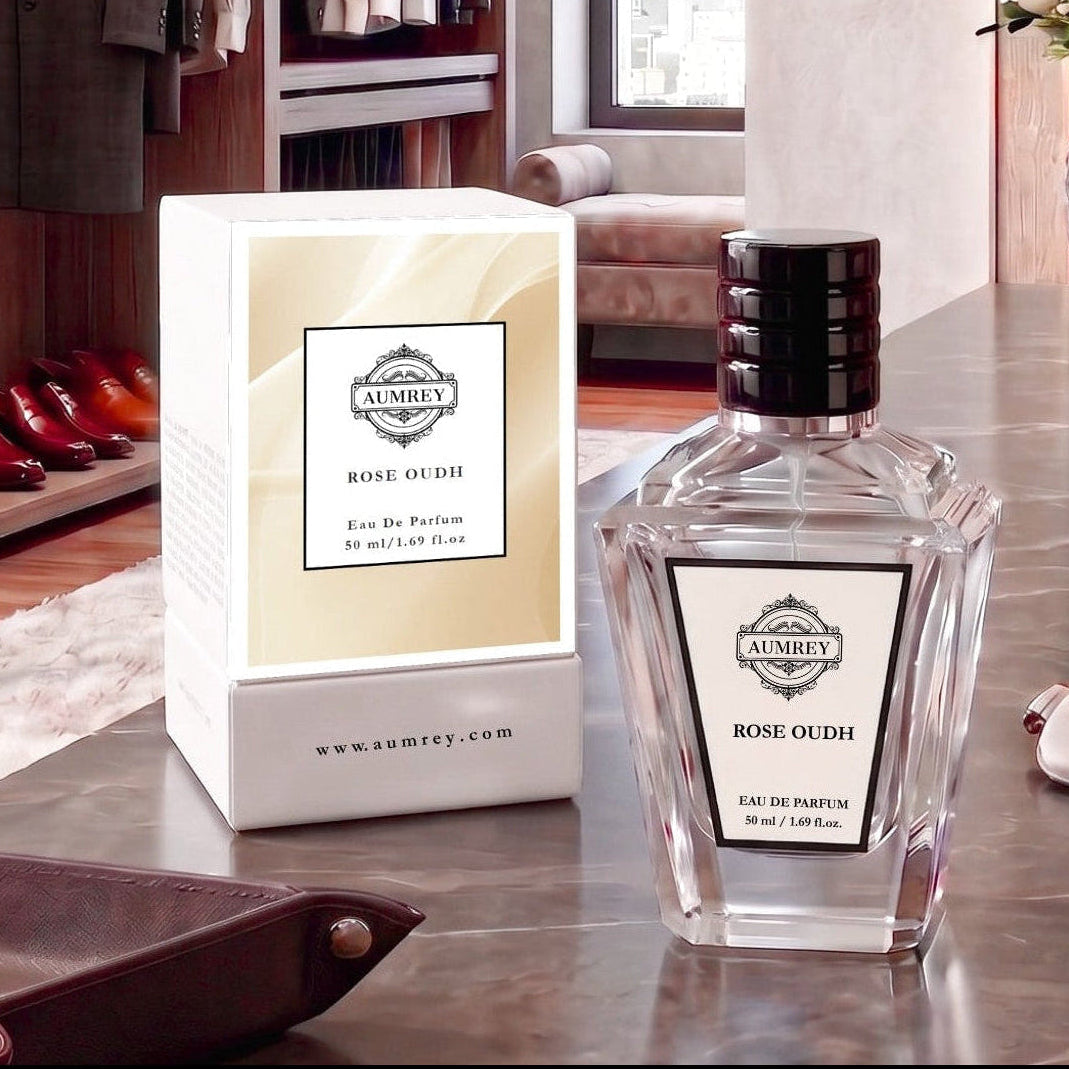 A bottle of Ambey Rose Oudh Eau De Parfum next to its white and beige packaging box, displayed on a polished marble countertop in a luxury dressing room setting.