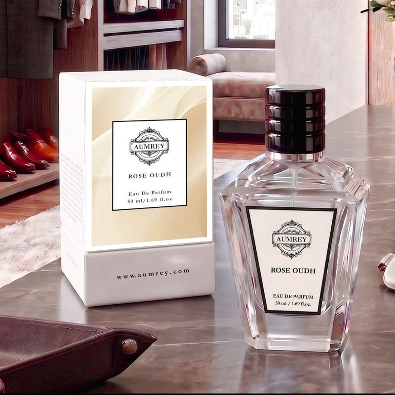 A bottle of Ambey Rose Oudh Eau De Parfum next to its white and beige packaging box, displayed on a polished marble countertop in a luxury dressing room setting.