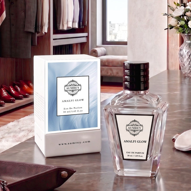 A bottle of Ambey Amalef Glow Eau de Parfum next to its white and light blue packaging box, displayed on a polished marble countertop in a luxury dressing room setting.