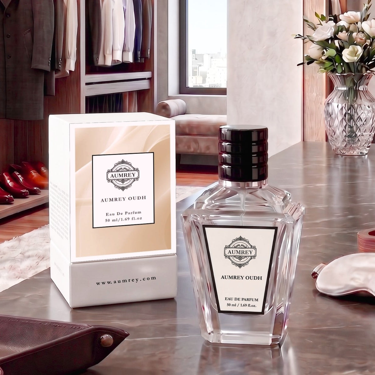 A clear glass perfume bottle labeled AUMREY OUDH with a black cap stands beside its white and beige box on a marble countertop in a styled room setting.