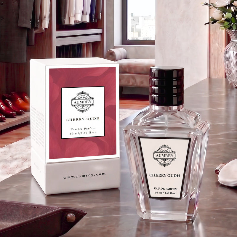 A bottle of Ambrey Cherry Oudh Eau De Parfum next to its white and red packaging box, set on a polished metallic table with a blurred dressing room background.