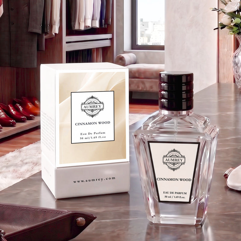 A bottle of Ambre Cinnamon Wood Eau De Parfum next to its white and beige packaging box, displayed on a dark wooden table in a luxurious room setting.