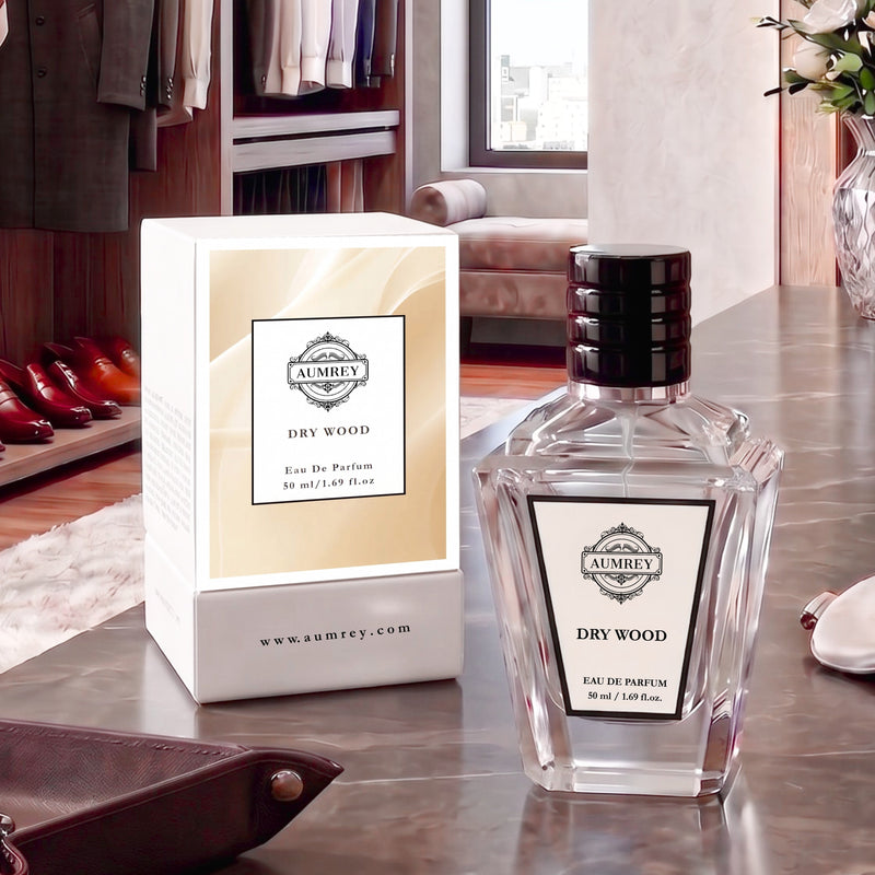 A clear glass perfume bottle labeled AUMNEY DRY WOOD Eau De Parfum next to its white and beige box, set on a polished metallic table in a stylish, modern room.