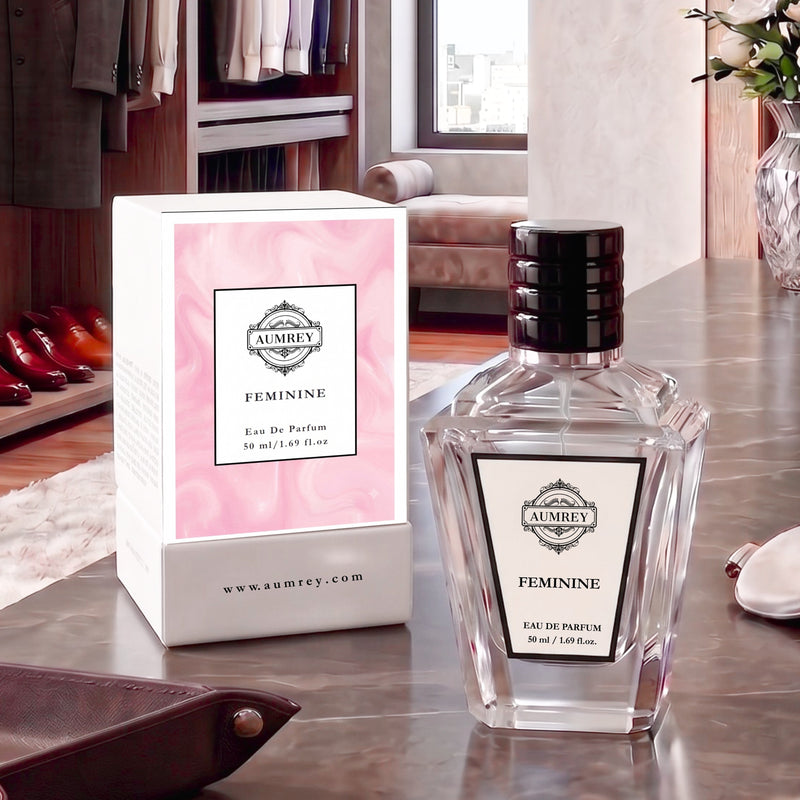 A bottle of Aubrey Feminine Eau De Parfum next to its pink and white box, displayed on a polished marble countertop in a luxury dressing room setting.
