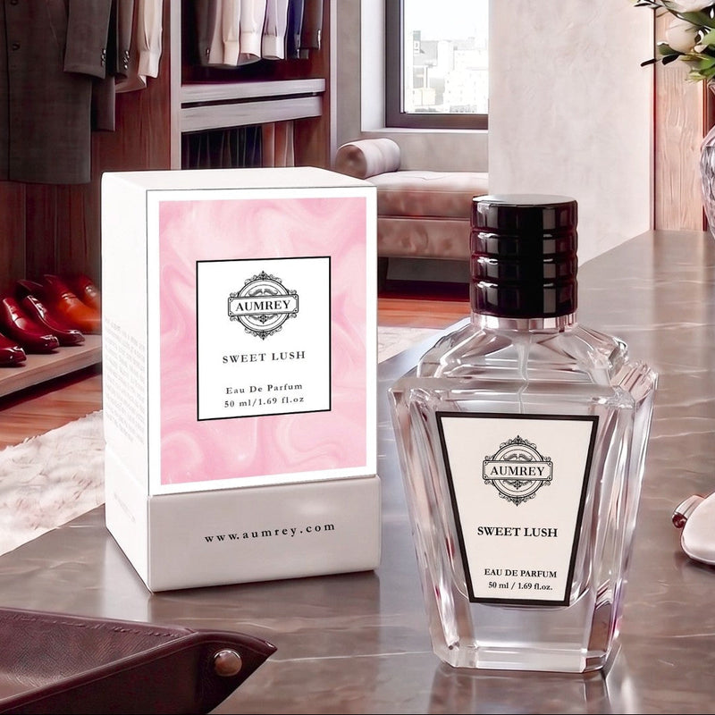 A bottle of Aumey Sweet Lush Eau De Parfum next to its pink and white box, displayed on a polished wooden table in a luxury dressing room setting.