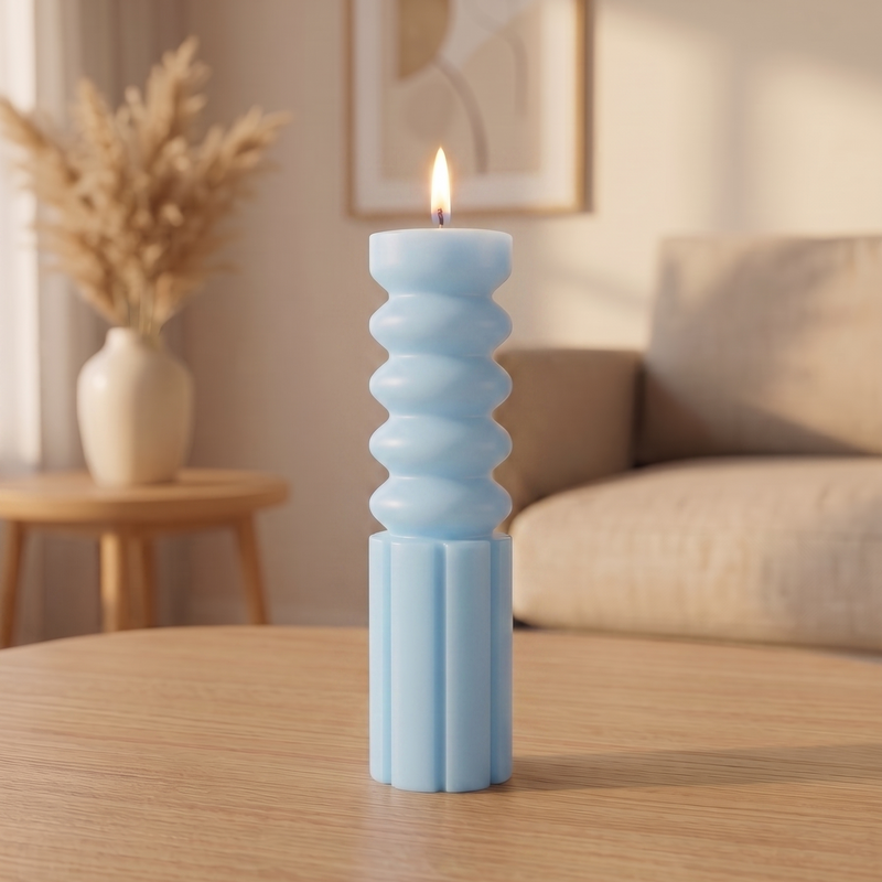 A light blue ribbed candle with a lit flame stands on a wooden table in a softly lit living room setting.
