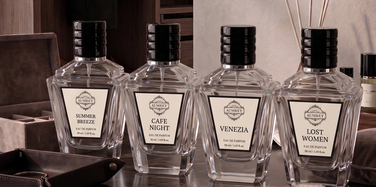 Four luxury cologne bottles with clear glass bodies and black caps are lined up on a dark marble surface in a high-end dressing room setting. The labels read 'SUMMER BREZZE', 'CAFE NIGHT', 'VENEZIA', and 'LOST WOMEN'.