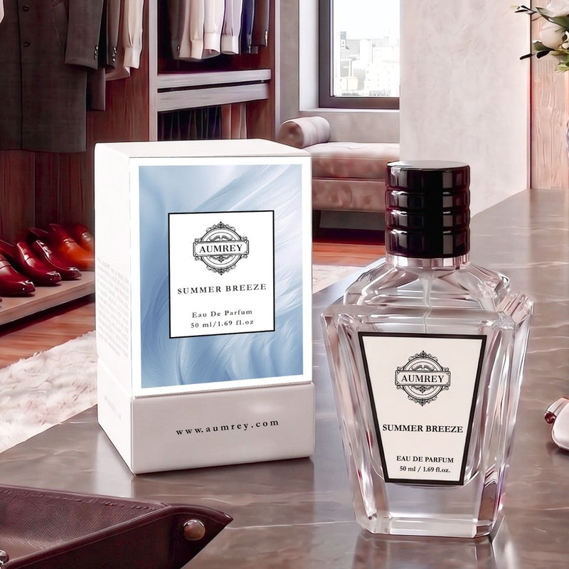 A clear glass perfume bottle labeled 'SUMMER BREEZE' by AUMAYI sits on a polished stone tabletop next to its white and light blue packaging box in a luxury interior setting.