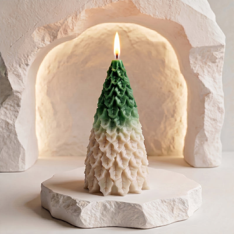 A tree-shaped candle with a green-to-cream gradient, lit and standing on a textured white stone base in front of a warm, stone-arch backdrop.